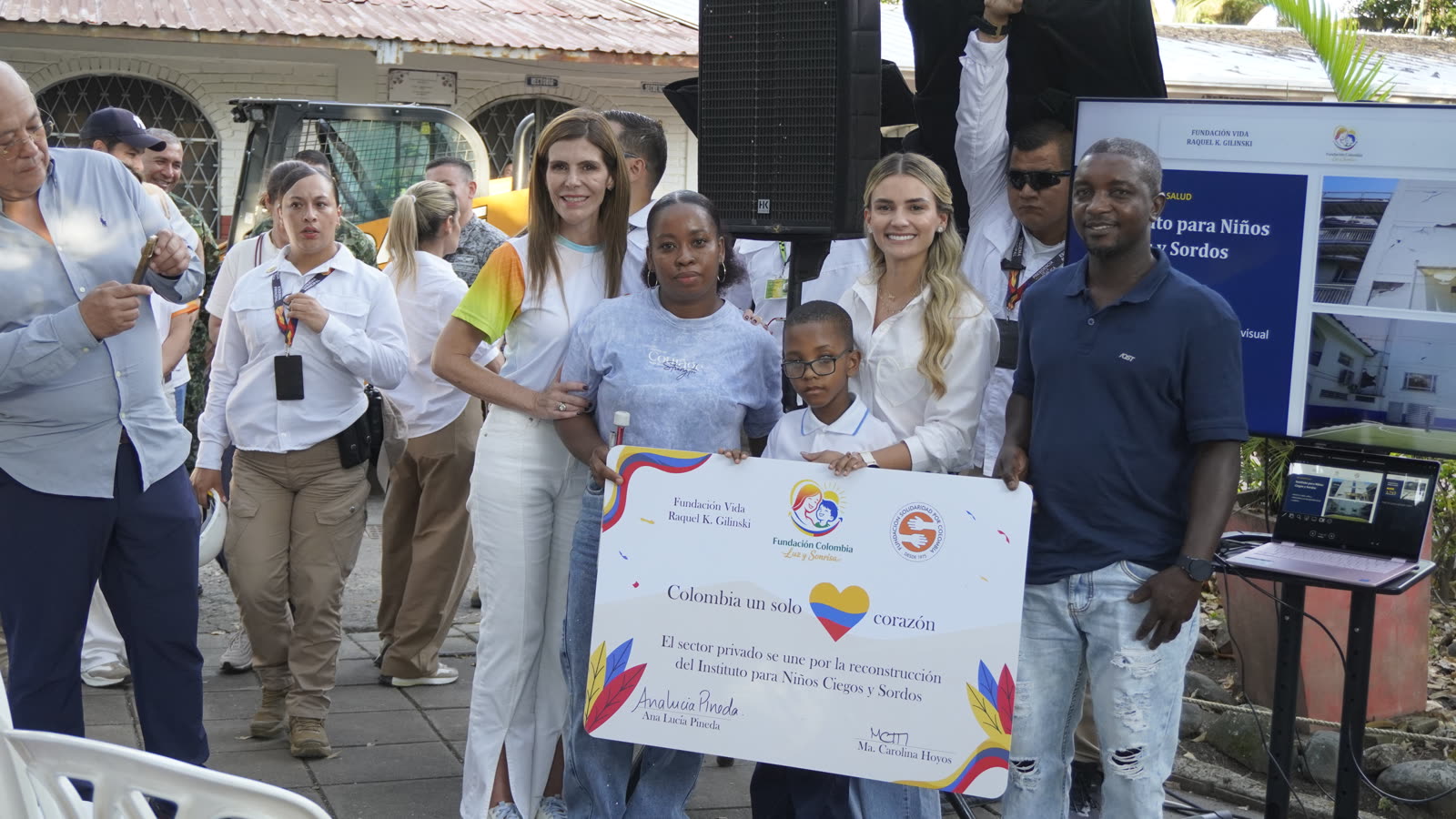 Entrega del cartel de la donación para el Instituto para Niños Ciegos y Sordos, acompañada por una familia de la institución